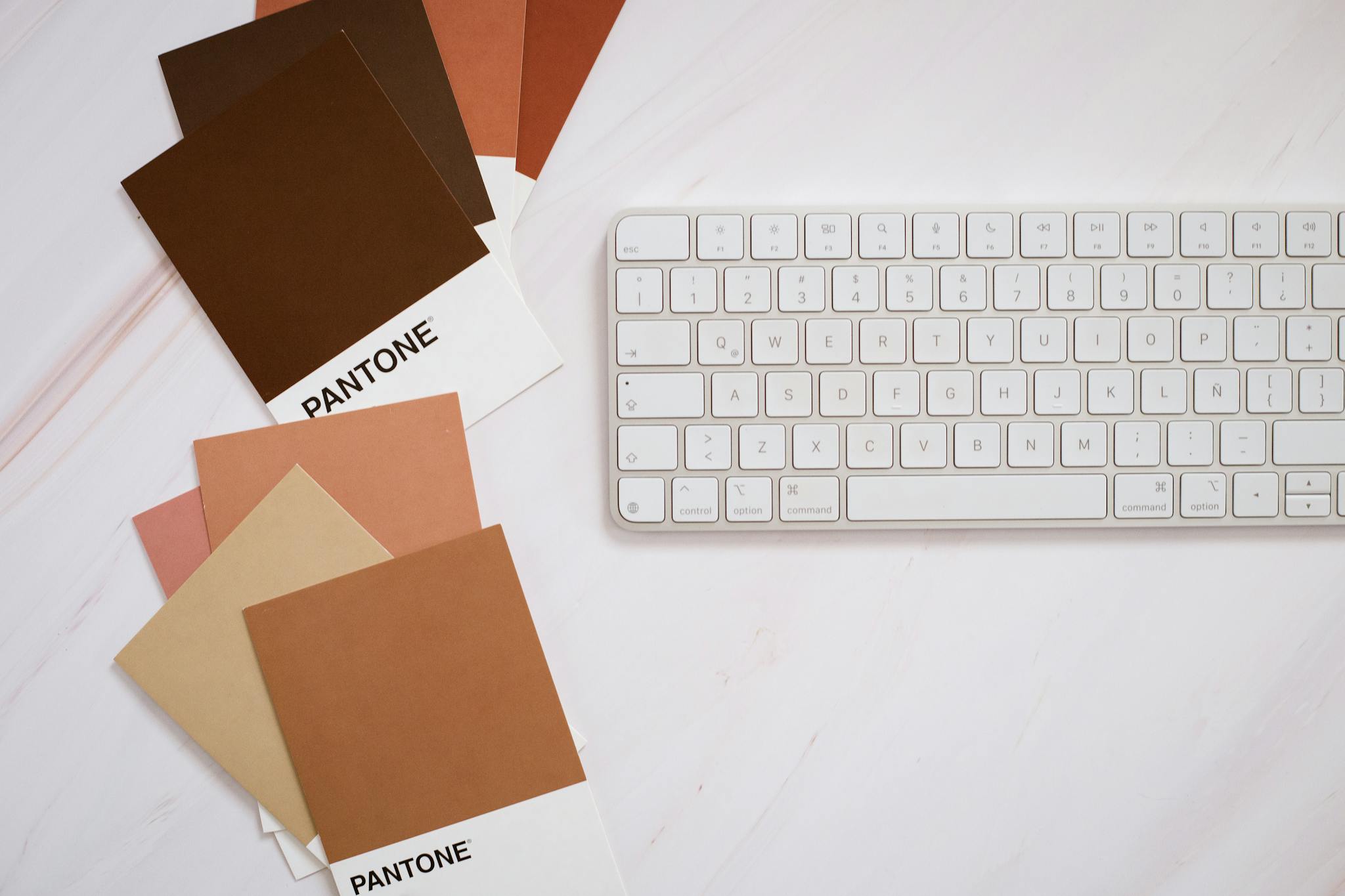 Stylish flat lay of Pantone color cards and keyboard on a white background.