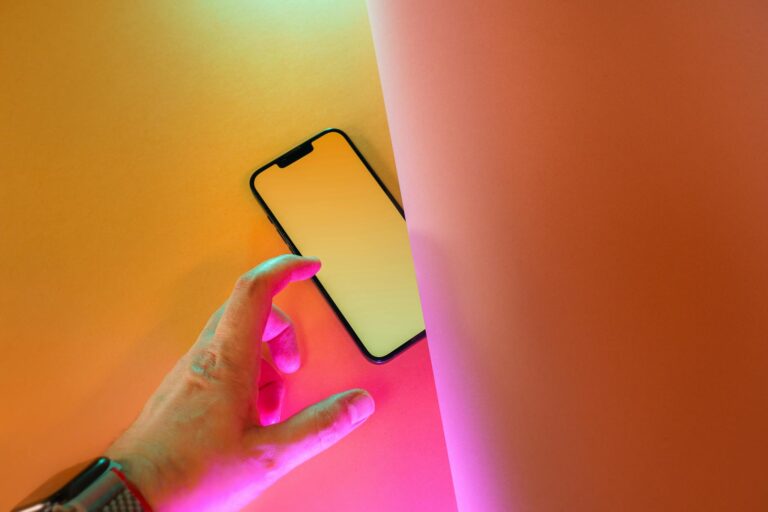 A hand reaching for a smartphone on a lively yellow and pink background, symbolizing connectivity.